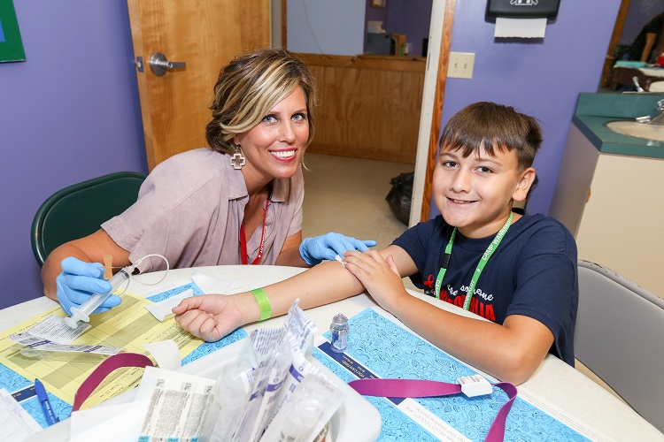 Outreach Nurse helps young boy with infusion at Camp Wannaklot