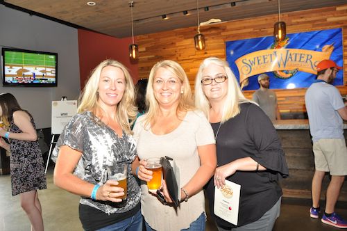 3 blond women in front of the sweetwater beer flag