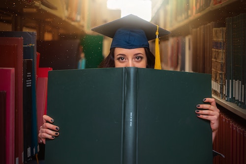 Woman in graduation gown and cap looking over a book