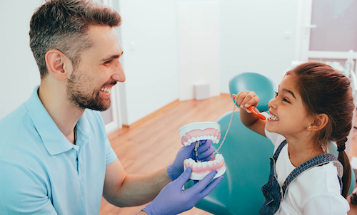 dentist teaching little girl how to floss